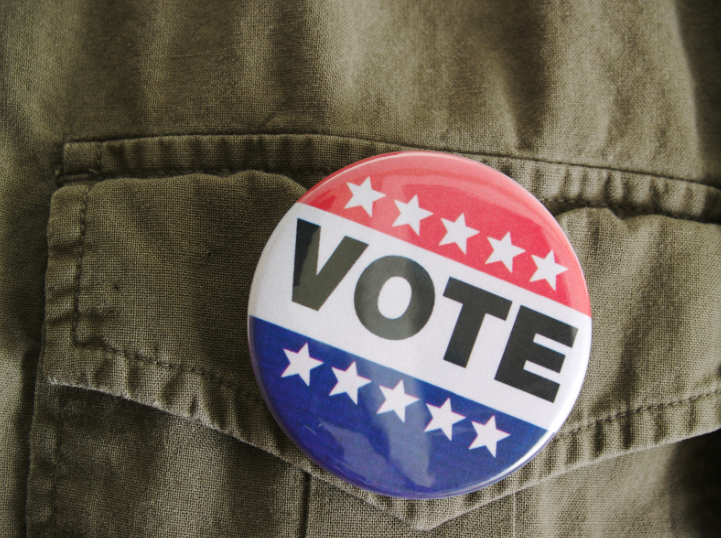 Red, white, and blue pin on a green shirt with the word VOTE 